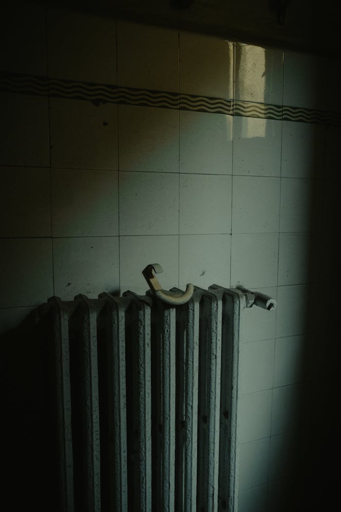 A moody shot of a vintage radiator on a tiled wall, emphasizing shadows and textures.